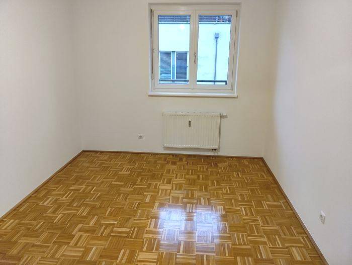 Freundliches Schlafzimmer mit Parkettboden und Fenster, das viel Tageslicht hereinlässt.