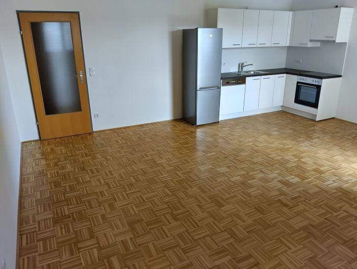 Offene Küche mit funktionaler Ausstattung, weißen Schränken und hellem Parkettboden.
