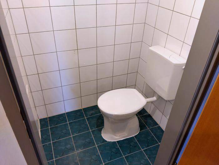 Separates WC mit weißen Wandfliesen und blauen Bodenfliesen.