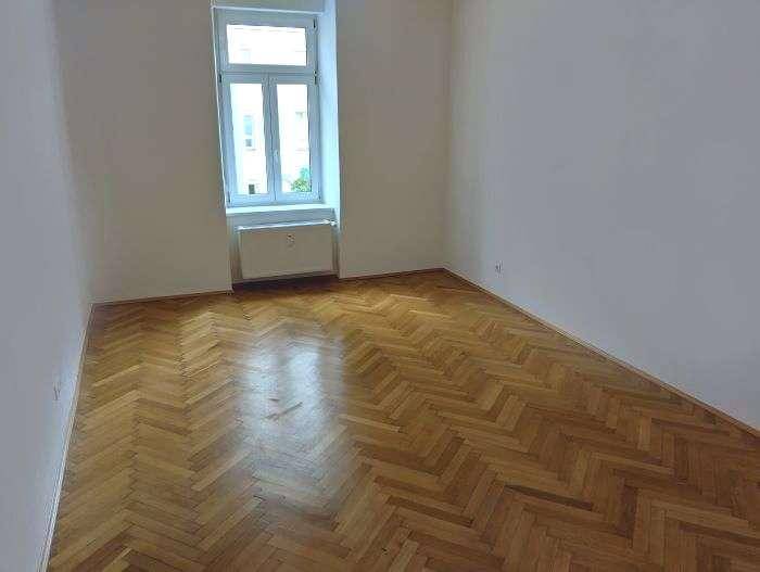 Freundliches Zimmer mit klassischem Fischgrätparkett und einem Fenster für Tageslicht.