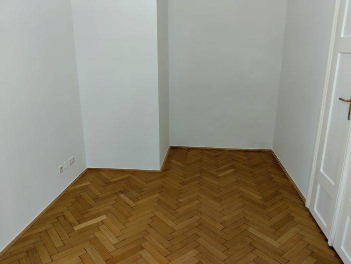 Leerer Raum mit elegantem Fischgrätparkett und weißer Tür, ideal für ein Schlafzimmer oder Büro.