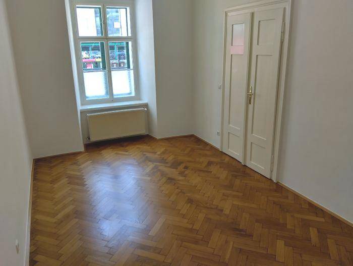Geräumiger Raum mit Fischgrätparkett, Fenster und Doppeltür, bietet vielseitige Nutzungsmöglichkeiten.