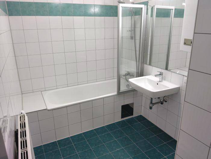 Badezimmer mit Badewanne, Waschbecken und hellen Fliesen, ausgestattet mit Duschwand.
