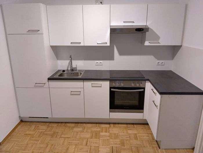 Funktionale Einbauküche mit weißen Schränken, dunkler Arbeitsplatte und integrierten Geräten.