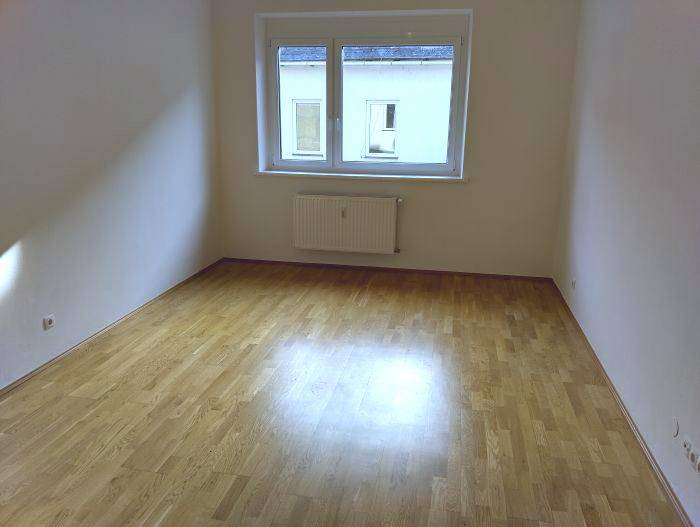 Heller, leerer Raum mit Parkettboden und Fenster zum Innenhof, ideal als Wohn- oder Schlafzimmer.