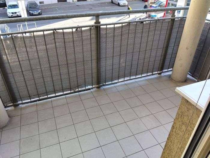 Balkon mit Fliesenboden und Blick auf die Straße, geschützt durch eine Sichtschutzwand.