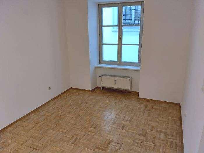 Helles Zimmer mit Parkettboden und Fenster, das viel Tageslicht hereinlässt.