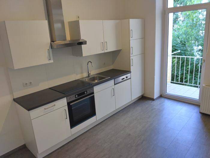 Moderne Einbauküche mit weißen Schränken, dunkler Arbeitsplatte und direktem Balkonzugang.