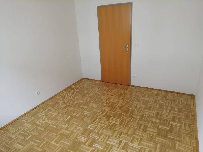 Schlichtes Schlafzimmer mit Parkettboden und einer Holztür, bietet vielseitige Nutzungsmöglichkeiten.