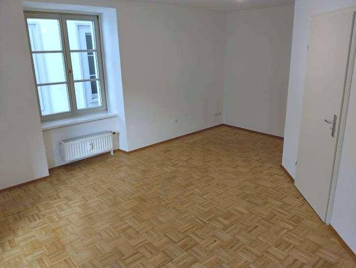 Geräumiges Zimmer mit Parkettboden, weiß gestrichenen Wänden und Fenster.