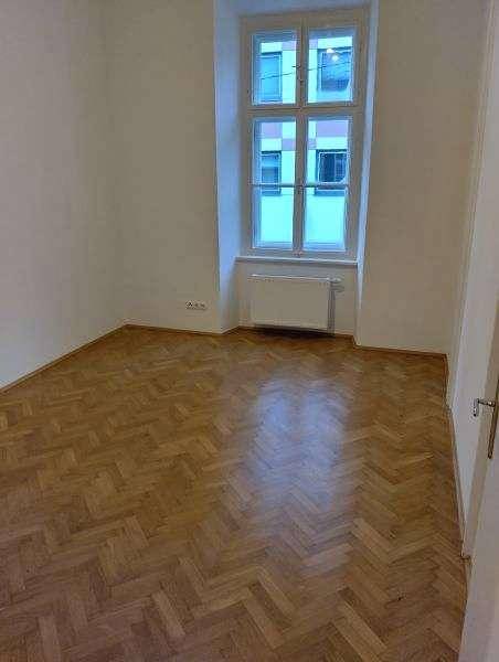 Gemütliches Zimmer mit Fischgrätparkett, einem Fenster und weiß gestrichenen Wänden.