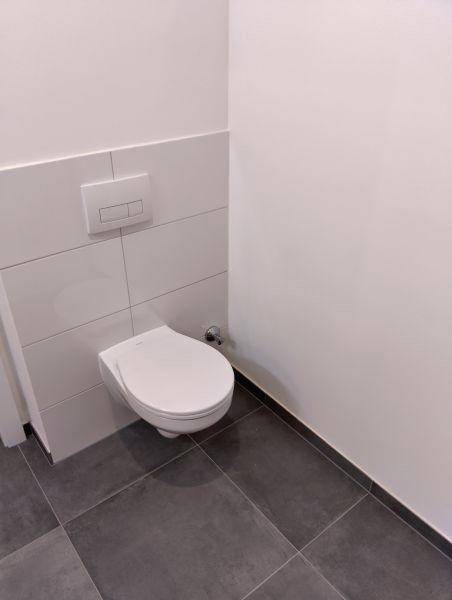 Wandhängendes WC mit weißer Keramik und dunklen Bodenfliesen in einem Badezimmer.