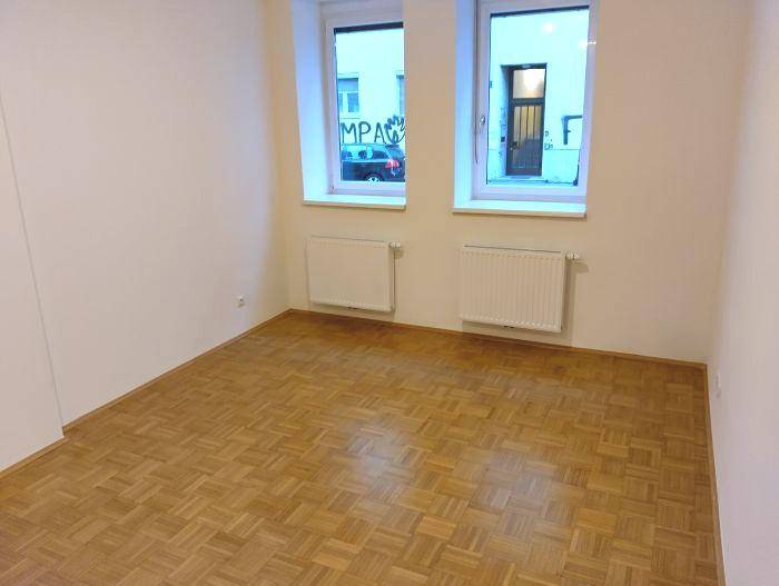 Leerer Raum mit Parkettboden, zwei Fenstern und Heizkörpern, blick auf die Straße.
