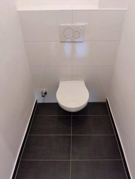 Gepflegtes Gäste-WC mit wandhängender Toilette, weißen Wandfliesen und dunklem Fliesenboden.