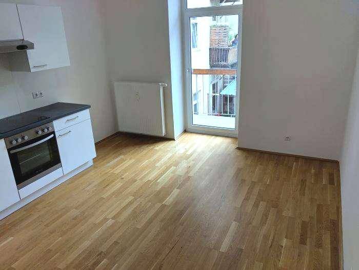 Helle Küchenzeile mit Balkonzugang, ausgestattet mit modernen Geräten und Holzplankenboden.