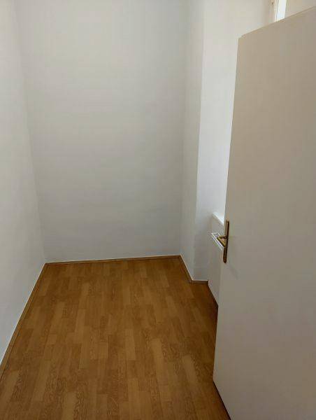 Kleiner, heller Raum mit Laminatboden und weißer Tür, vielseitig nutzbar als Abstellraum oder Büro.