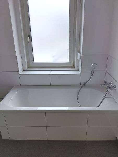 Helles Badezimmer mit Badewanne und einem Fenster, das für natürliche Belüftung sorgt.