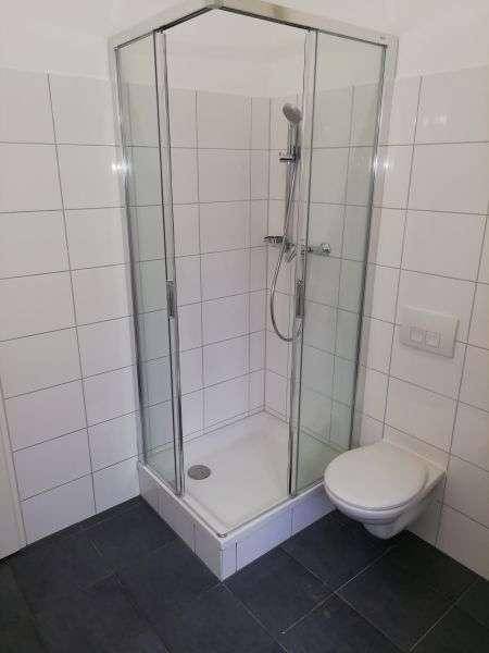Badezimmer mit Eckdusche und wandhängendem WC, dunkle Bodenfliesen und weiße Wandfliesen.