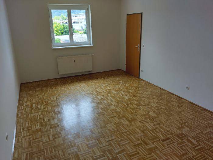 Geräumiges Zimmer mit hellem Parkettboden, weißen Wänden und Fenster mit Blick ins Grüne.