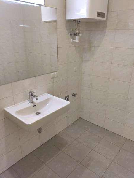 Modernes Badezimmer mit Wandwaschbecken, großem Spiegel und hellen Fliesen an Wänden und Boden.