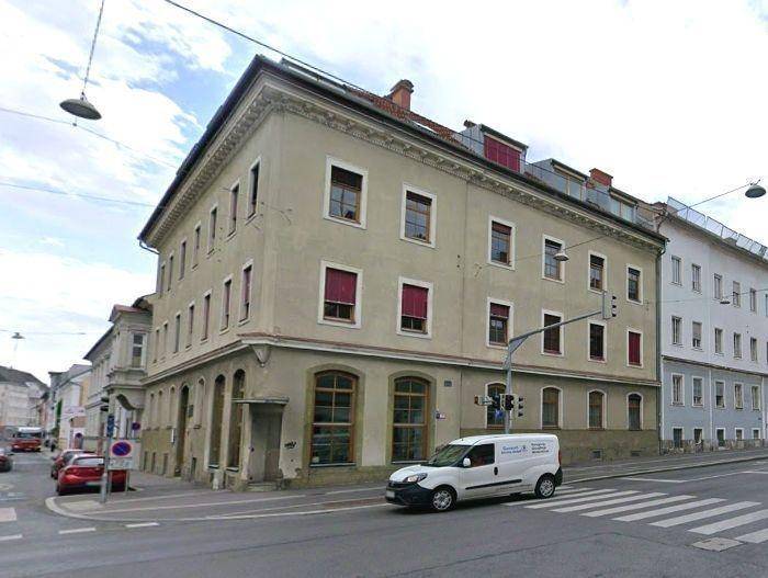 Historisches Eckgebäude an einer städtischen Kreuzung mit klassischer Architektur und roten Fensterläden.