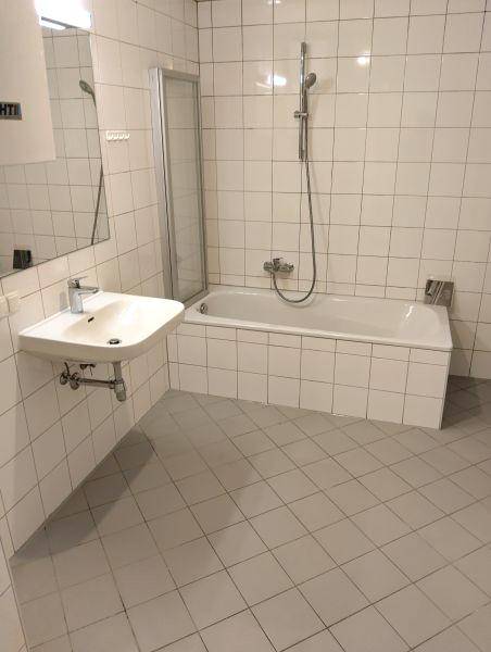 Helles Badezimmer mit weißen Fliesen, Badewanne mit Duschabtrennung und Einzelwaschbecken.
