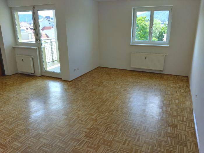 Heller Wohnraum mit Parkettboden, Zugang zum Balkon und Blick ins Grüne.