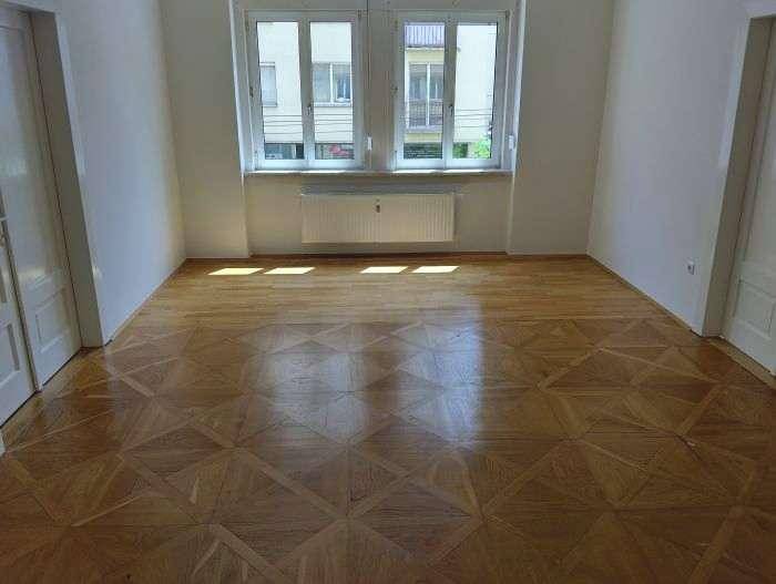 Geräumiger, unmöblierter Raum mit Parkettboden und großen Fenstern, ideal für individuelle Einrichtung.