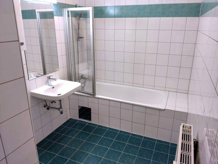 Badezimmer mit Badewanne, Duschabtrennung, Waschbecken und blauen Bodenfliesen.