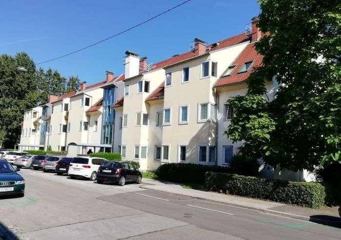 Ansicht der Wohnanlage von der Straße mit geparkten Autos und grüner Bepflanzung.