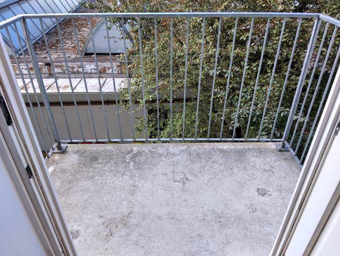 Kleiner Balkon mit Metallgeländer und Blick auf Bäume und Dächer.