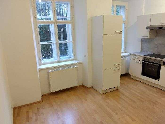 Heller Küchenbereich mit Fenster, Heizkörper und hellem Holzfußboden, gut beleuchtet.