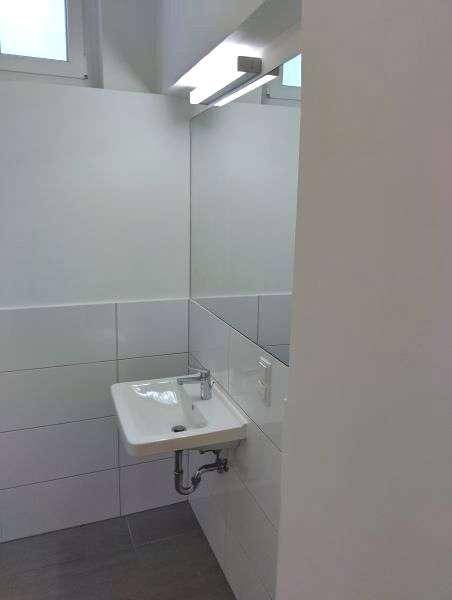 Funktionales Badezimmer mit Waschbecken, großem Spiegel und Fenster für Tageslicht.