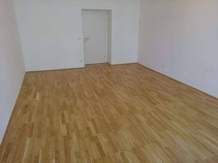 Geräumiges Zimmer mit hellem Holzplankenboden und einer schlichten weißen Tür.