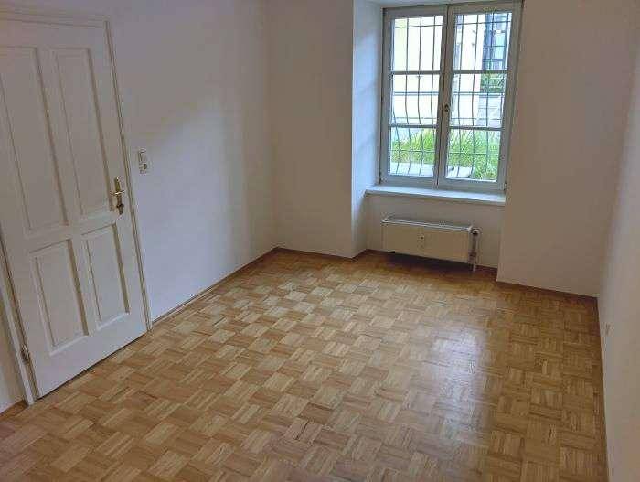 Helles Zimmer mit Parkettboden, weißer Tür und Fenster mit Blick nach draußen.