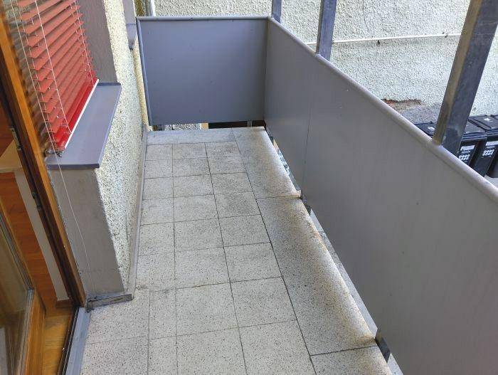 Kleiner Balkon mit Fliesenboden und grauer Brüstung, ideal für eine gemütliche Sitzecke.