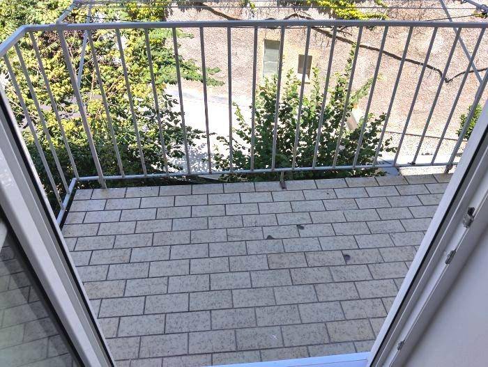 Kleiner Balkon mit Fliesenboden und Blick auf den begrünten Innenhof.
