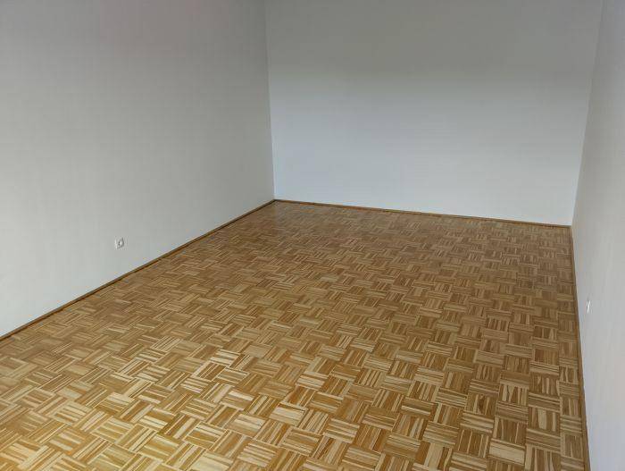 Leerer Raum mit hellem Parkettboden und weißen Wänden, bereit zur individuellen Gestaltung.
