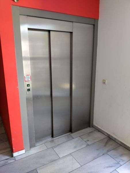 Moderner Aufzug in einem Flur mit gefliestem Boden und roter Wand.