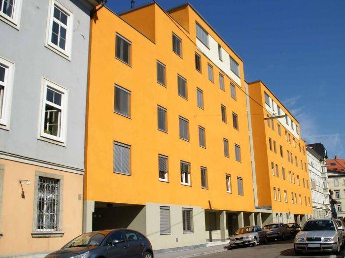 Modernes Mehrfamilienhaus mit leuchtend oranger Fassade und zahlreichen Fenstern.