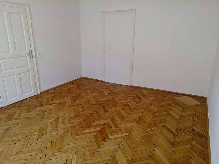 Heller Raum mit gepflegtem Fischgrätparkett und einer schlichten weißen Tür, bereit für neue Bewohner.