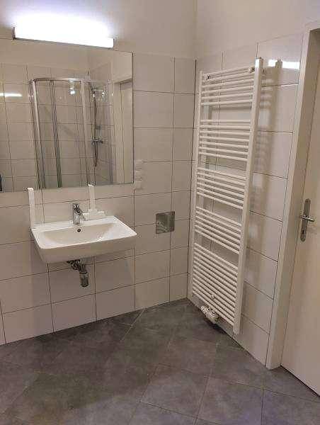 Modernes Badezimmer mit weißen Wandfliesen, grauen Bodenfliesen und Duschkabine.