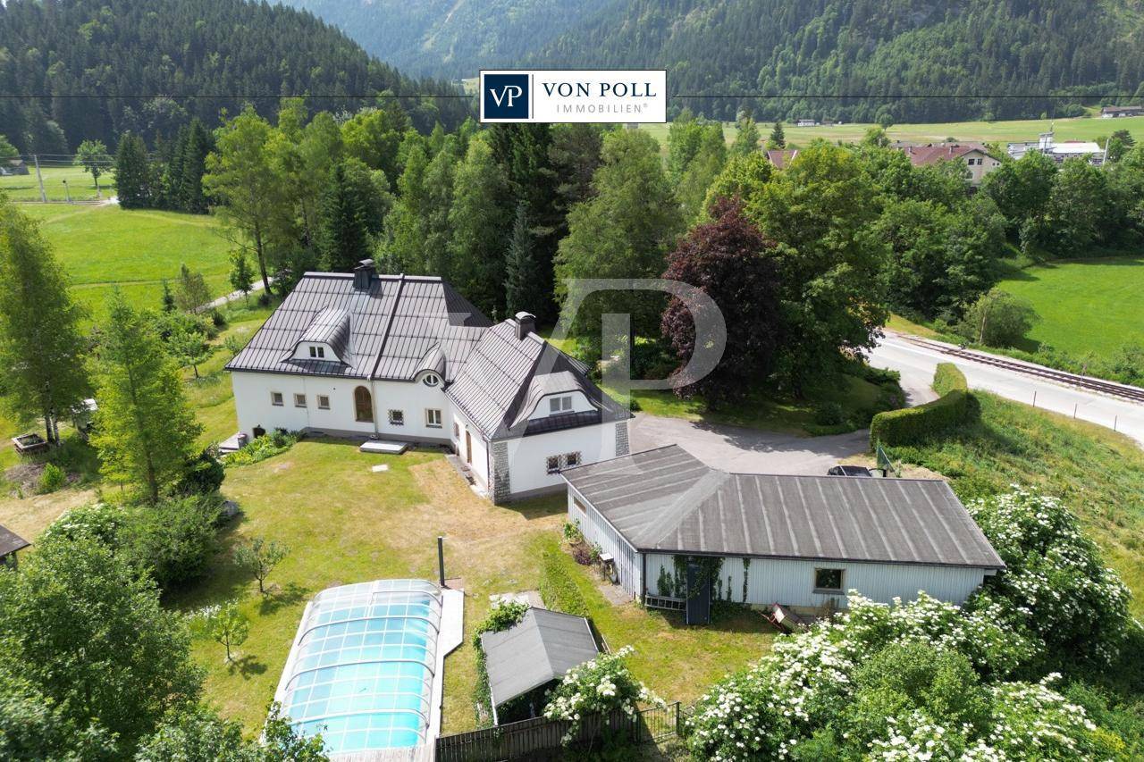 Luftaufnahme des Anwesens mit Haupthaus, Nebengebäude und Poolbereich vor grüner Bergkulisse.