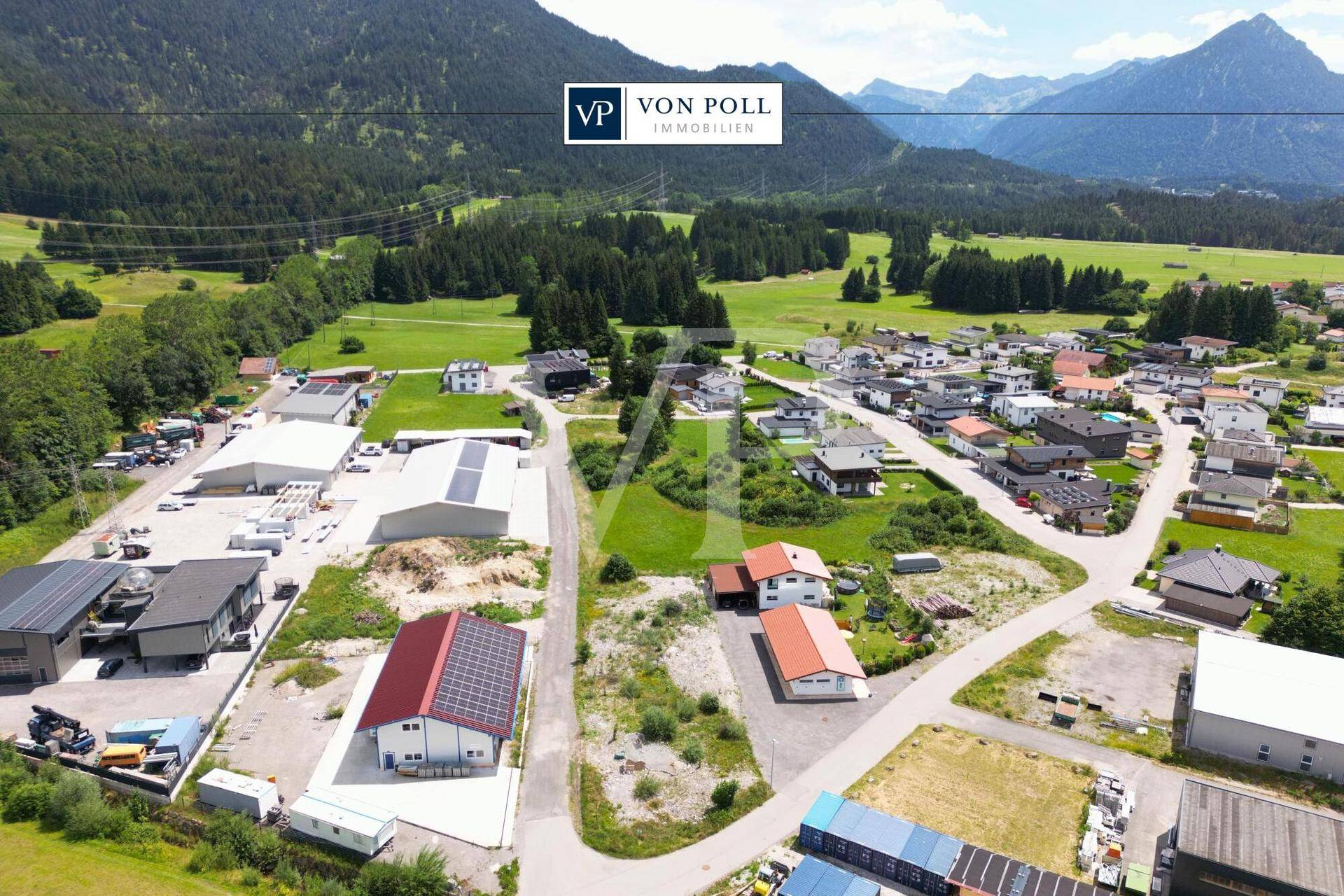 Weitläufige Luftaufnahme einer gemischten Wohn- und Gewerbegegend mit viel Grün und Bergpanorama.