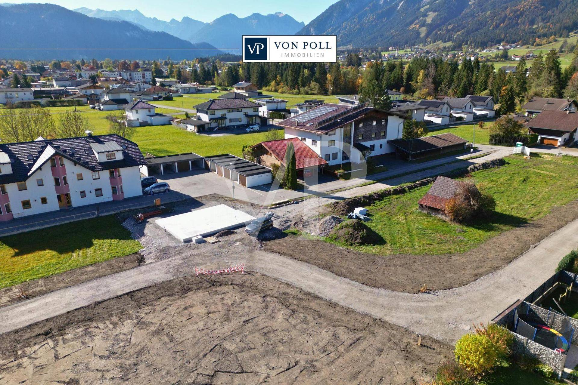Panoramablick auf ein Baugebiet mit See- und Bergsicht sowie einer vorbereiteten Baufläche.