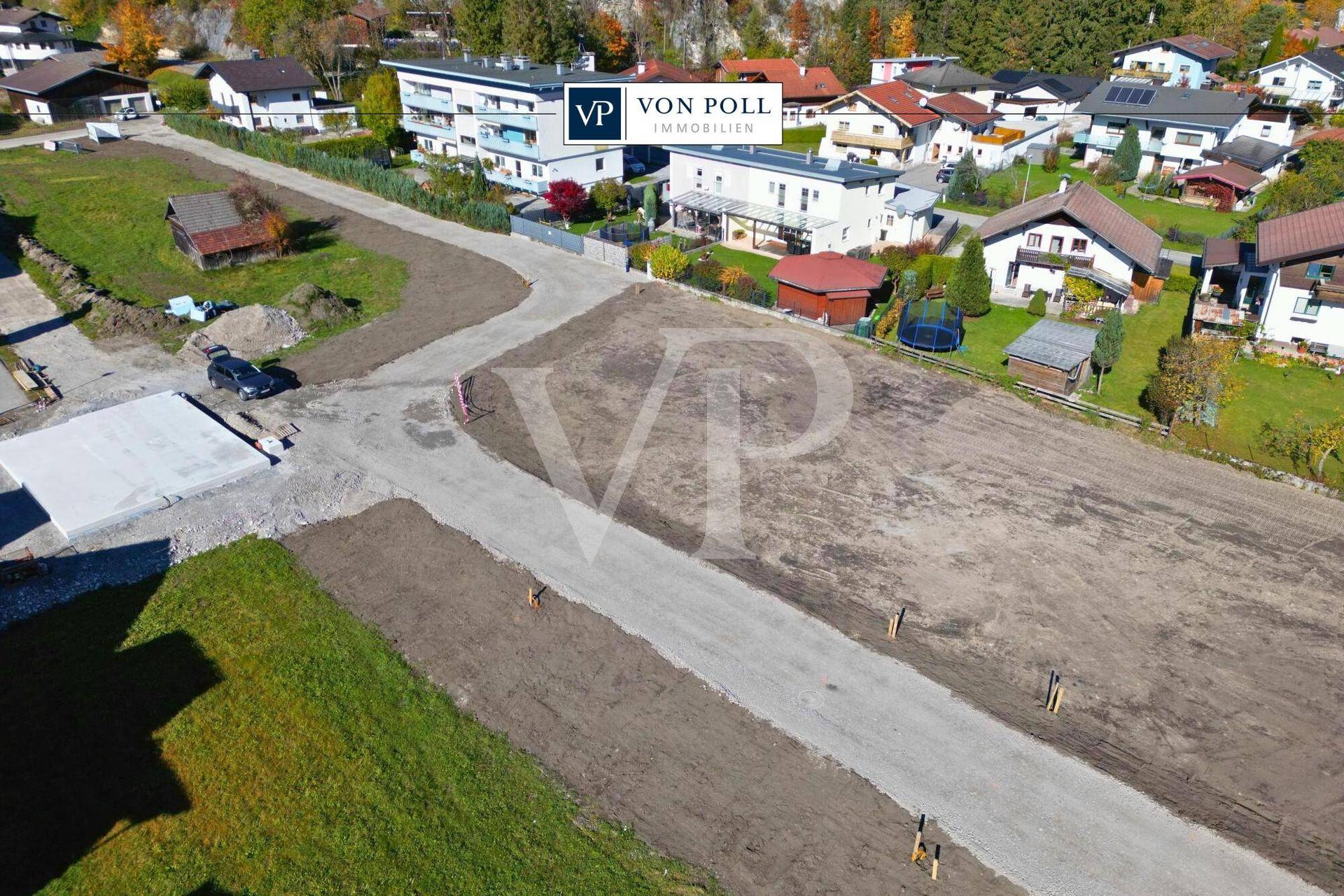 Luftaufnahme eines erschlossenen Baugrundstücks mit neuer Zufahrtsstraße, umgeben von bestehenden Wohnhäusern.