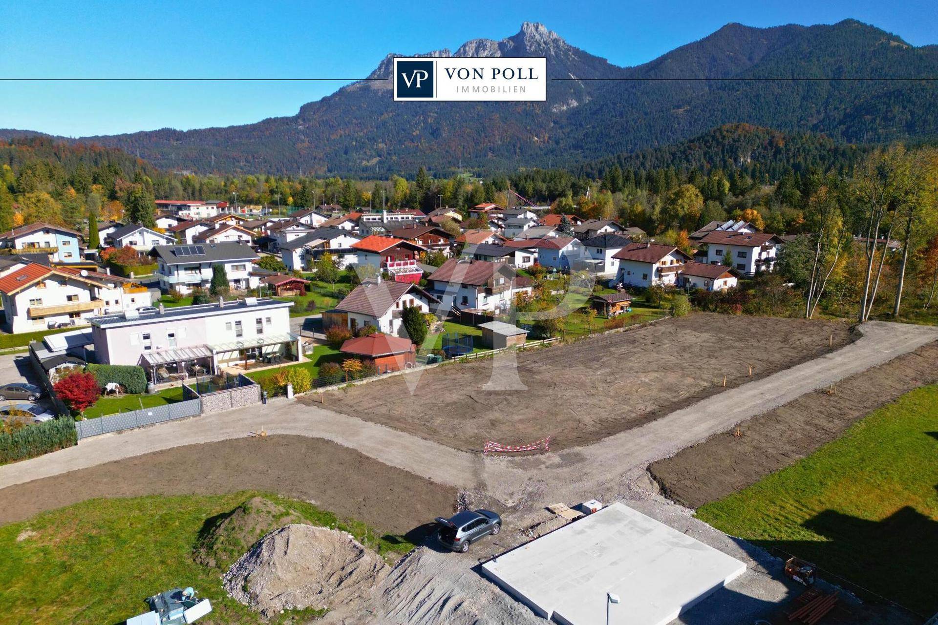 Panoramablick auf eine Wohnsiedlung mit unbebauten Grundstücken und einer beeindruckenden Berglandschaft im Hintergrund.