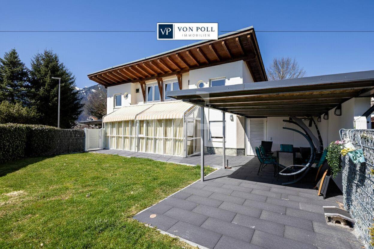 Gepflegter Garten mit Rasenfläche, überdachtem Sitzbereich und Carport.