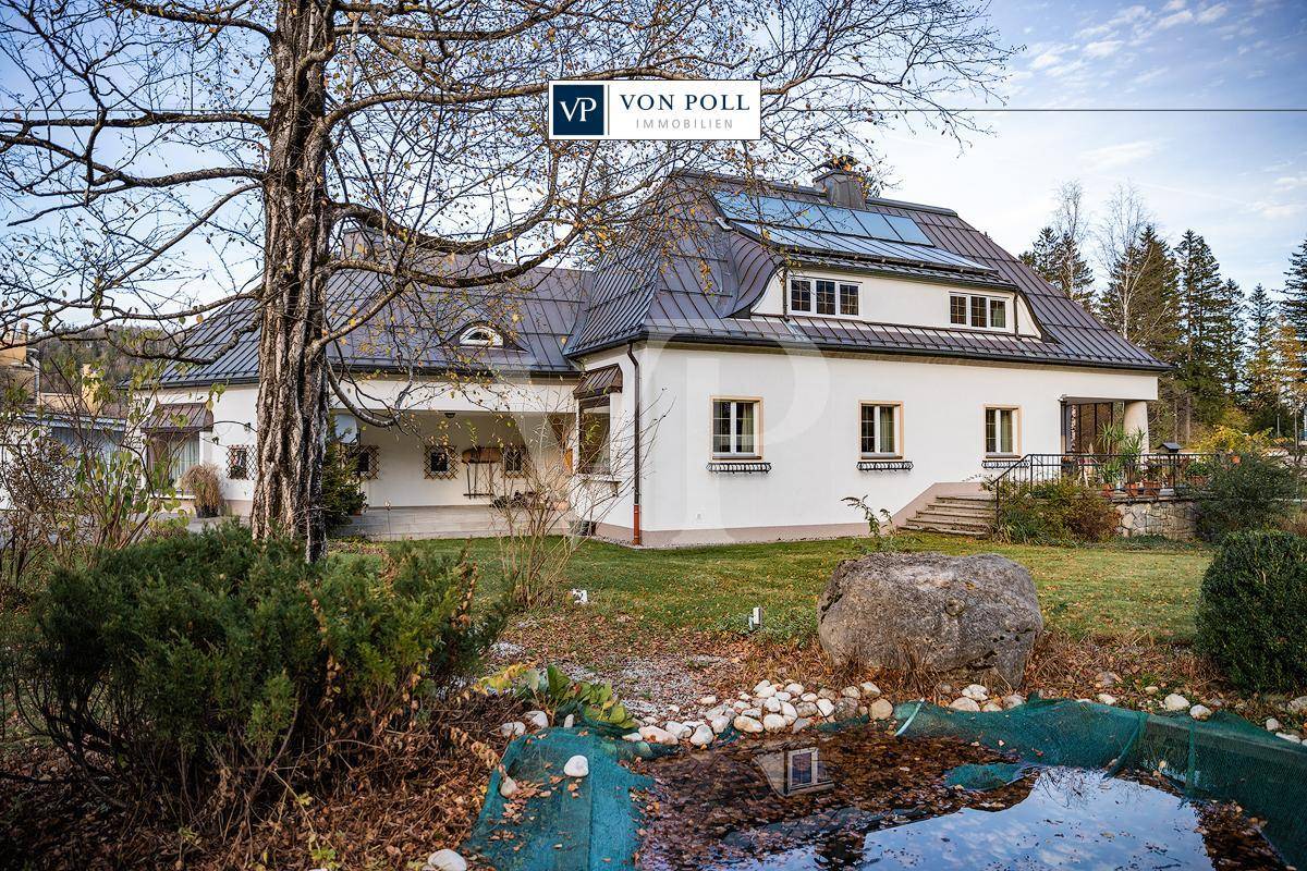 Idyllisches Landhaus mit weißer Fassade, großem Garten und Teich, umgeben von Bäumen.