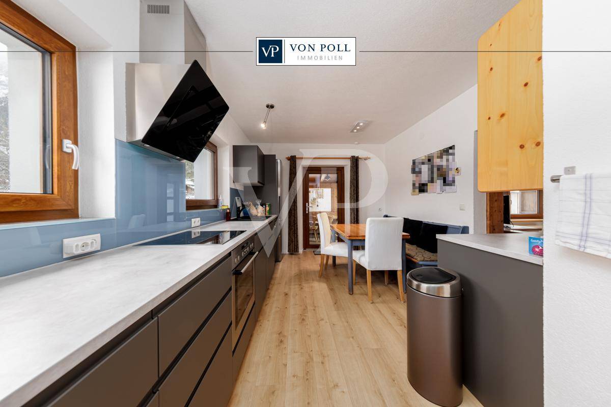 Moderne Küche mit dunklen Schränken, Induktionskochfeld und integriertem Essbereich mit Holzboden.